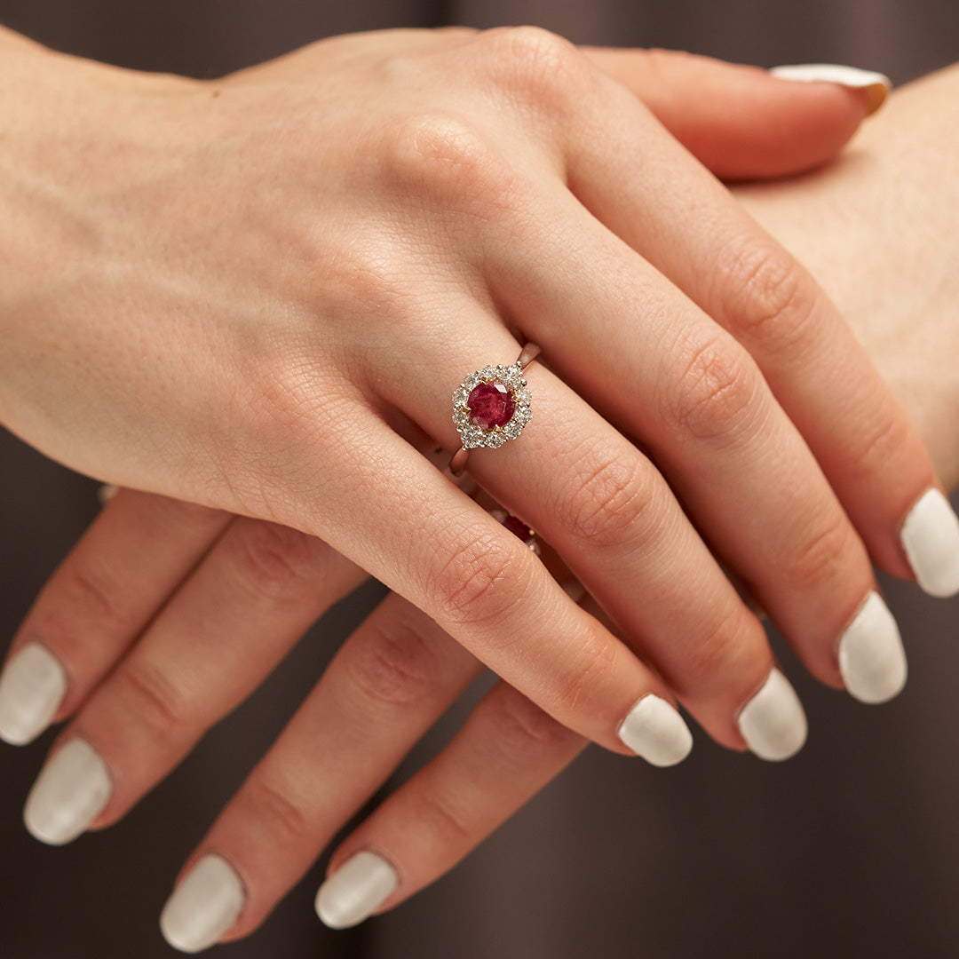 Graceful woman showcasing a luxurious round Red Emerald ring encircled by a sparkling diamond halo, highlighting the gem's rich color and brilliance, featured at Park City Jewelers.