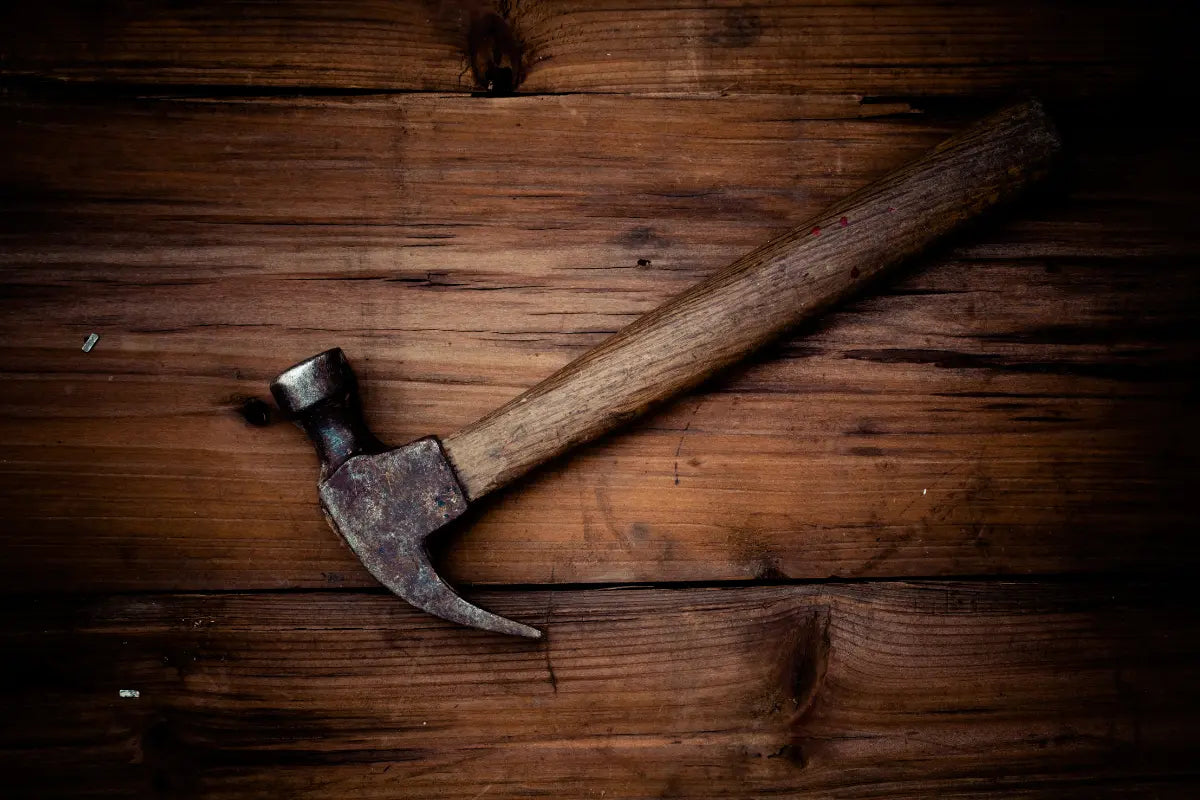 A hammer laying on a wooden bench.