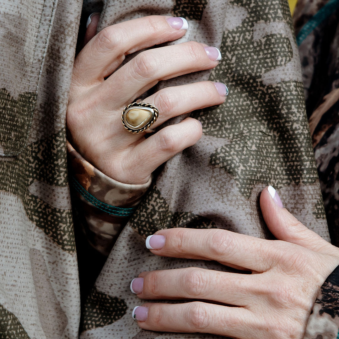 A woman's hand gracefully wrapped around a man's arm, showcasing an intricate elk ivory ring with a unique braided accent, symbolizing a story of adventure and connection - Park City Jewelers.