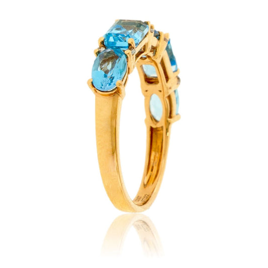 Angled view of a mixed-cut blue topaz and diamond ring in 14K yellow gold, highlighting the row of five main gemstones.