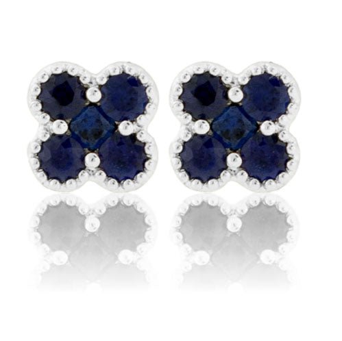 A pair of 18K white gold clover stud earrings, set with deep blue round sapphires and featuring a detailed milgrain edge.