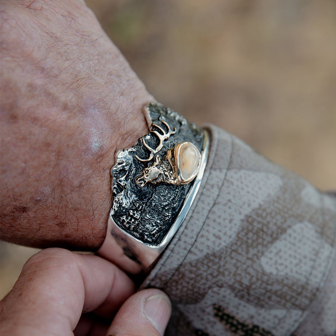 A man wearing the custom elk ivory and mountain scene cuff bracelet on his wrist, with a camouflage jacket sleeve visible.