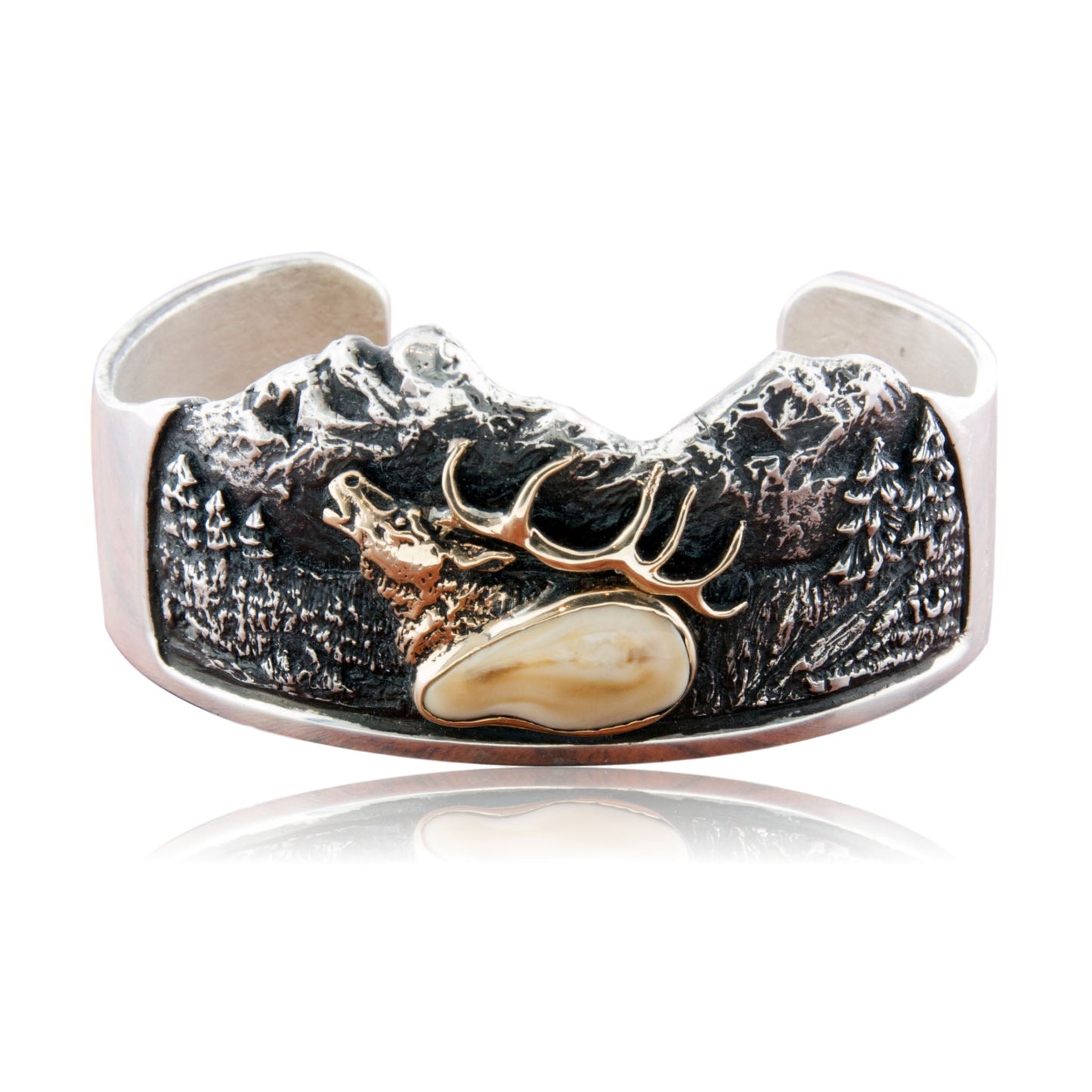 A wide sterling silver cuff bracelet with a detailed, oxidized mountain scene, featuring a 14K yellow gold elk head and a bezel-set elk ivory.