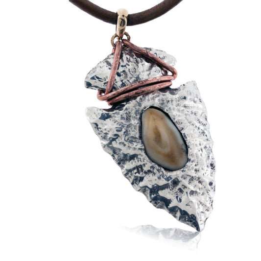 A large, hammered sterling silver arrowhead pendant featuring a bezel-set elk ivory and a rustic, wrapped copper wire accent, hanging from a black rubber cord.