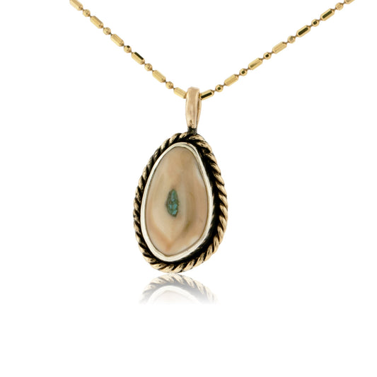 A 14K yellow gold elk ivory pendant with a braided halo, featuring a vibrant turquoise inlay in the center of the ivory, on a gold chain.
