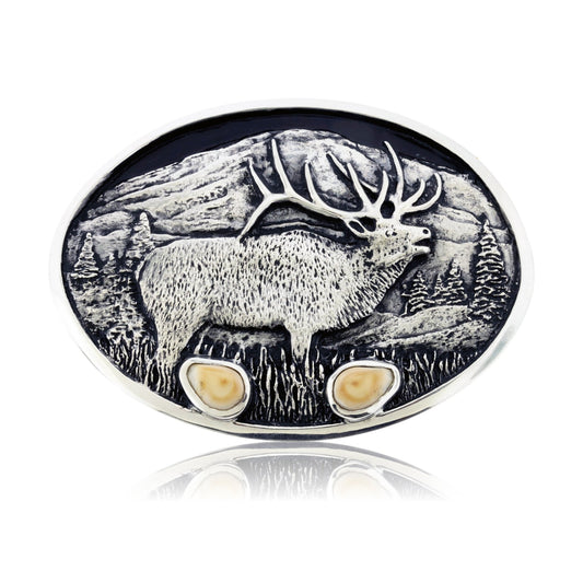 An oval sterling silver belt buckle featuring a three-dimensional sculpture of a bull elk standing in a detailed mountain landscape, with two bezel-set elk ivories at the base.