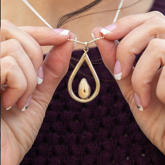 A woman with a french manicure holding the sterling silver teardrop elk ivory pendant up to her chest.