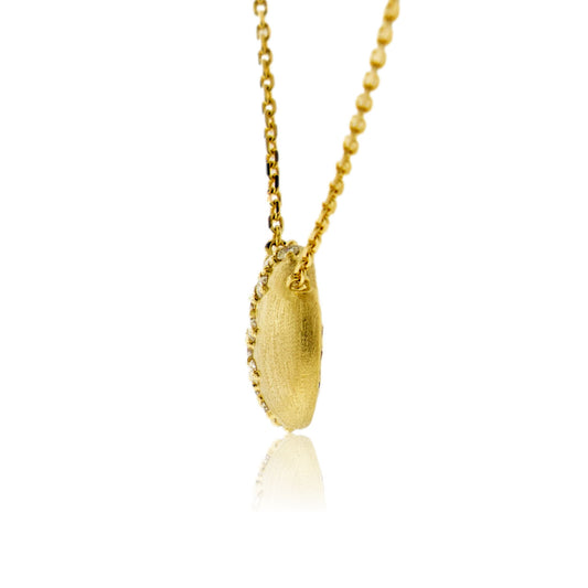A side profile view of the satin-finished 14K gold domed diamond pendant, showing its thickness and the diamonds set along the curve.