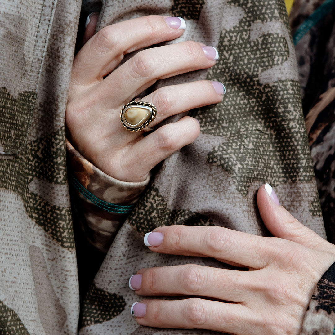 A woman's hand gracefully wrapped around a man's arm, showcasing an intricate elk ivory ring with a unique braided accent, symbolizing a story of adventure and connection.
