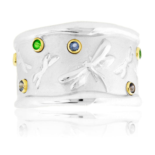 A wide, sand-blasted sterling silver band featuring polished dragonflies and bezel-set green tsavorite and blue sapphire gemstones in 14K yellow gold.
