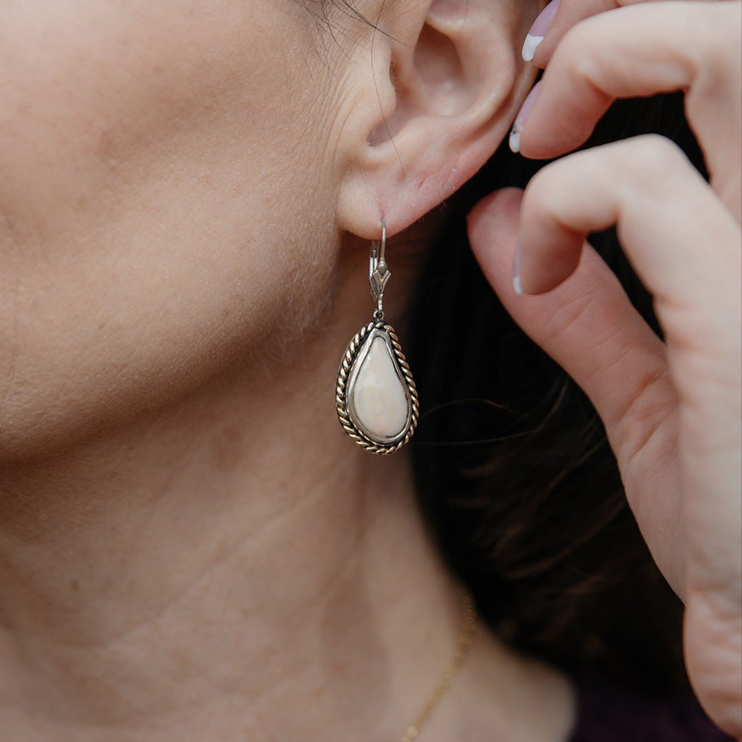 A woman wearing a two-tone elk ivory dangle earring, showing the braided gold and silver design hanging from her ear.