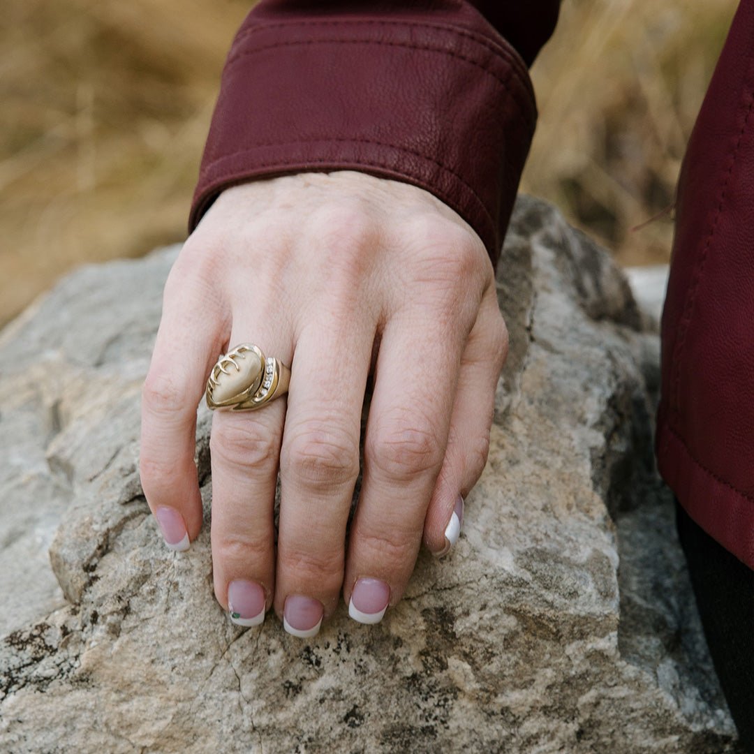 A woman's hand resting on a rock, wearing the yellow gold version of the asymmetrical elk ivory and diamond antler ring.